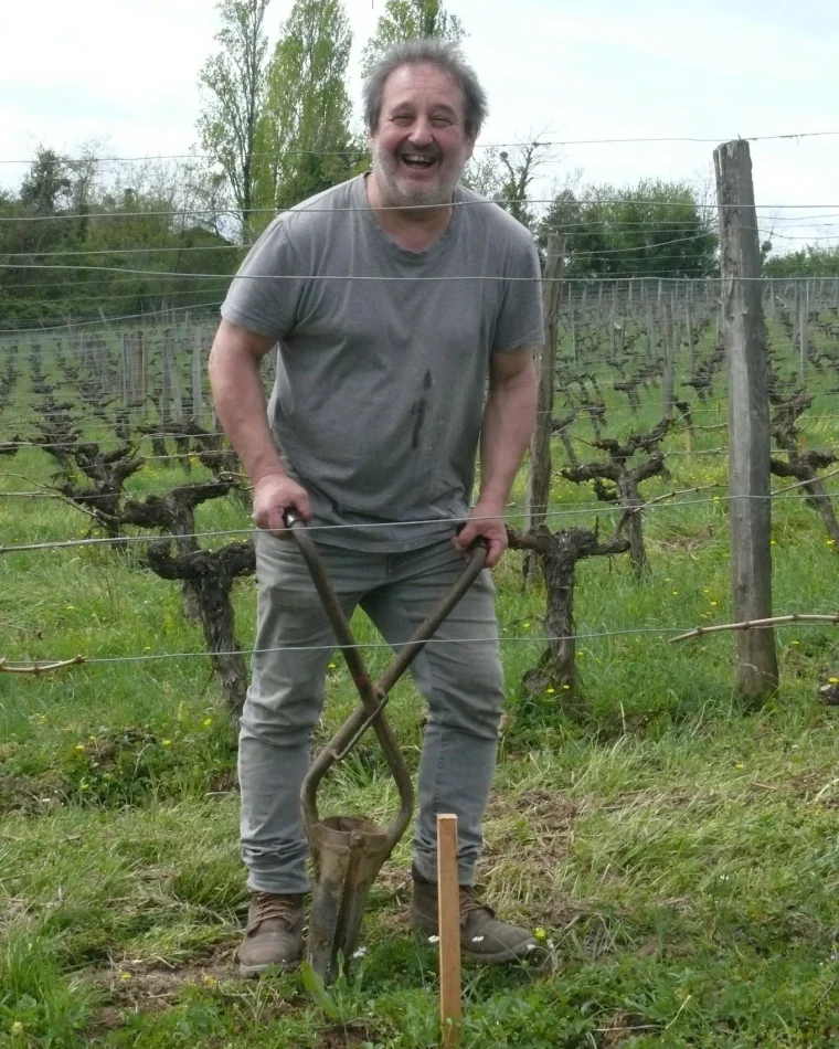 Norbert Depaire, riant, une bêche plantée devant lui, entre deux rangs de vigne au printemps